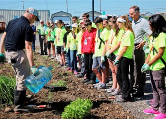 Tony Eallonardo (left), scientist at O’Brien & Gere, demonstrates how to water new plantings.  Honeywell Syracuse Program Director John McAuliffe (right) listens along with students.